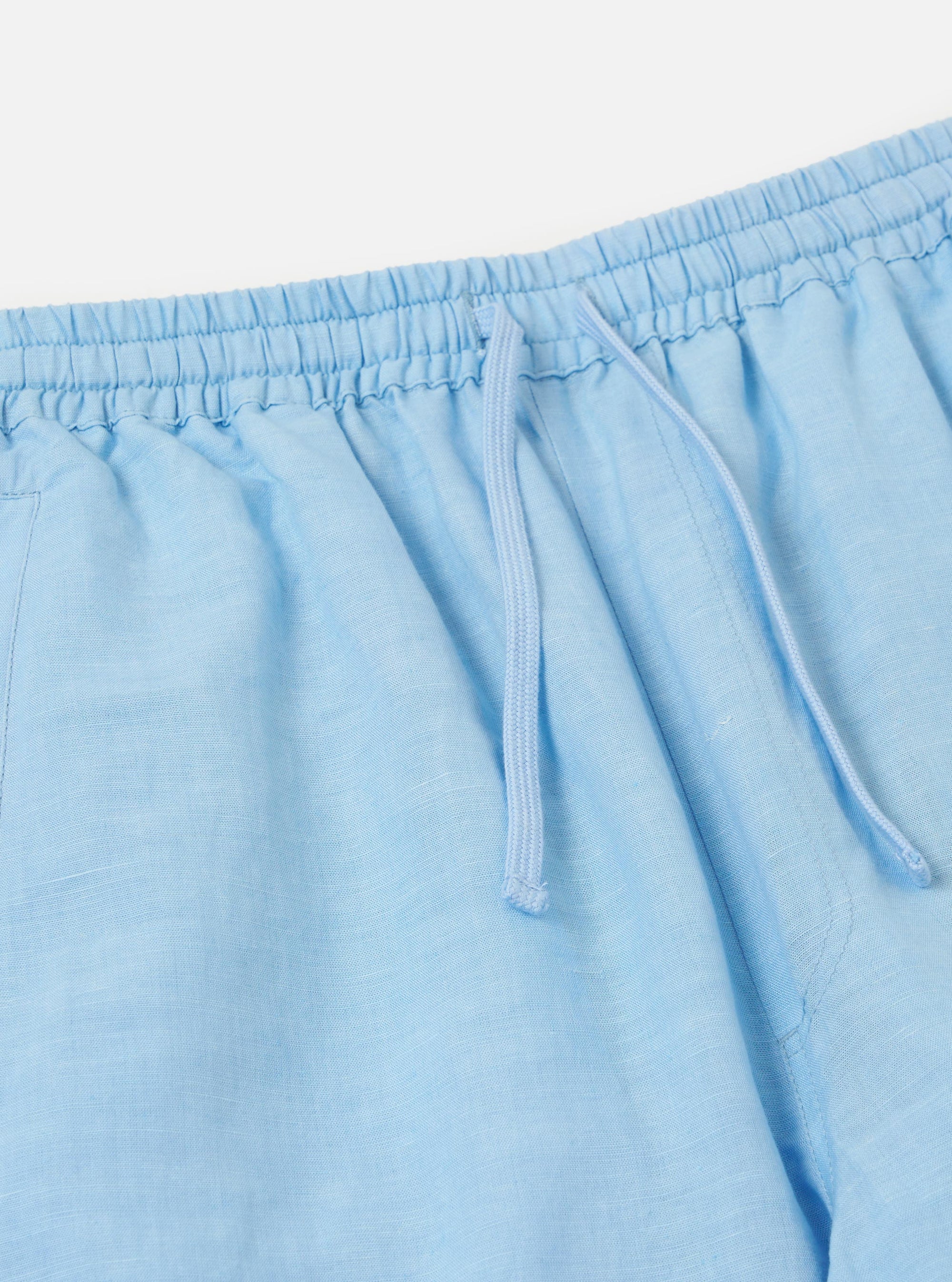 A pair of pale blue linen cotton shirting parachute pants is displayed flat against a plain white background. The garment features a relaxed, straight-leg fit and an elasticated drawstring waistband.