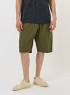 A model is wearing the Olive Broadcloth Vacation Short against a plain white background. The image shows the shorts from the waist down, highlighting the olive green cotton fabric, a relaxed fit, and a side slip pocket. The model is standing straight and the garment is paired with dark-colored shoes.