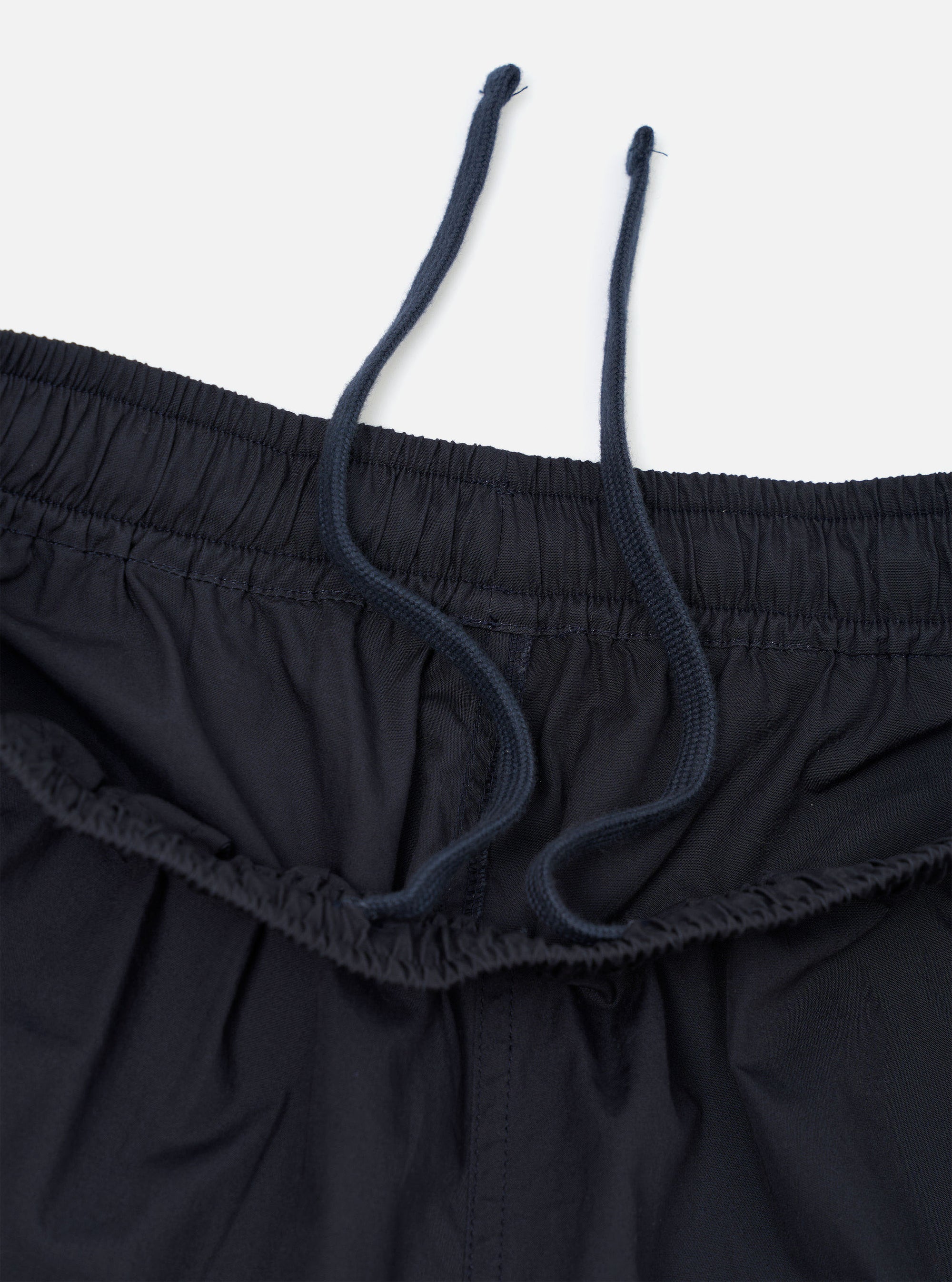 A pair of Navy Broadcloth Vacation Shorts is shown from a close-up perspective, highlighting the texture of the navy blue cotton fabric and the stitching details of a pocket. The garment is laid flat against a plain white background.