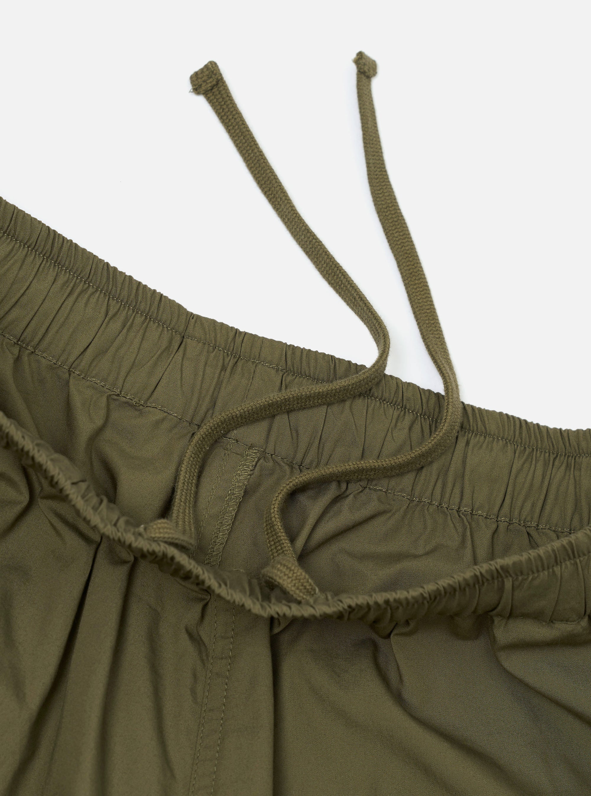 A pair of olive green cotton broadcloth vacation shorts is shown laid flat against a solid white background. The shorts feature a relaxed, wide-leg cut, an elasticated waistband with a drawstring, and side slip pockets.