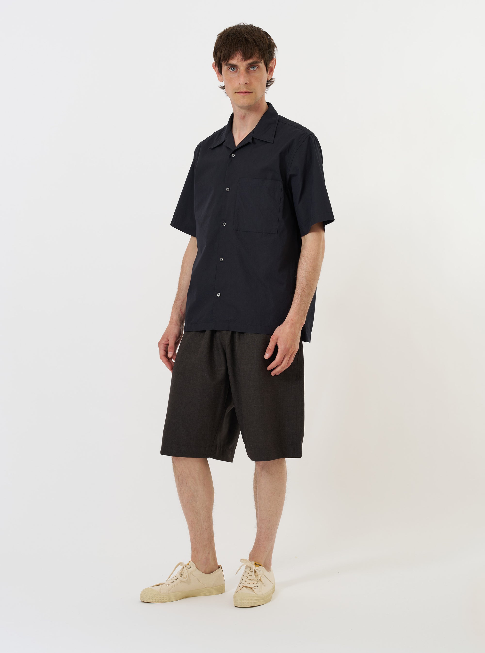 The Navy Broadcloth Camp Shirt is shown from the back, laid flat against a plain white background. The image highlights the horizontal back yoke, short sleeves, and a straight hem with small side slits.
