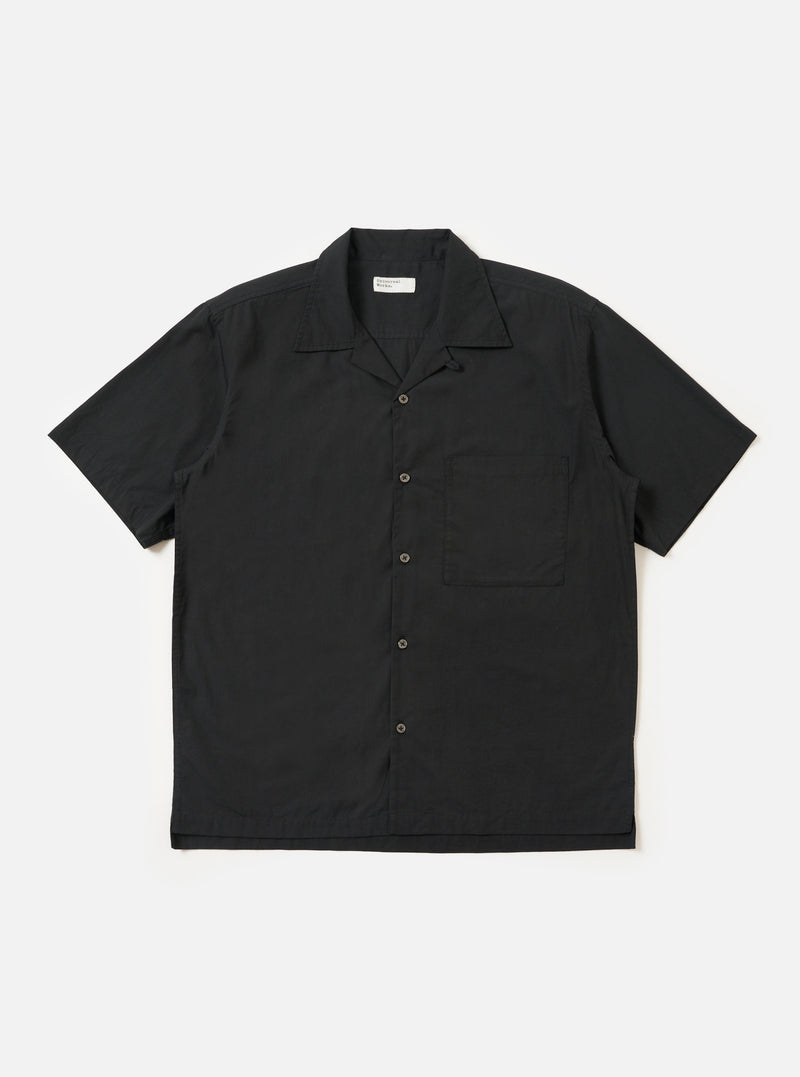 The Black Broadcloth Camp Shirt is shown laid flat against a solid white background. The shirt features a one-piece camp collar, a button-down front, and a single large chest pocket on the left side. The short-sleeve garment is made from a smooth, black broadcloth cotton fabric.