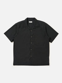 The Black Broadcloth Camp Shirt is shown laid flat against a solid white background. The shirt features a one-piece camp collar, a button-down front, and a single large chest pocket on the left side. The short-sleeve garment is made from a smooth, black broadcloth cotton fabric.