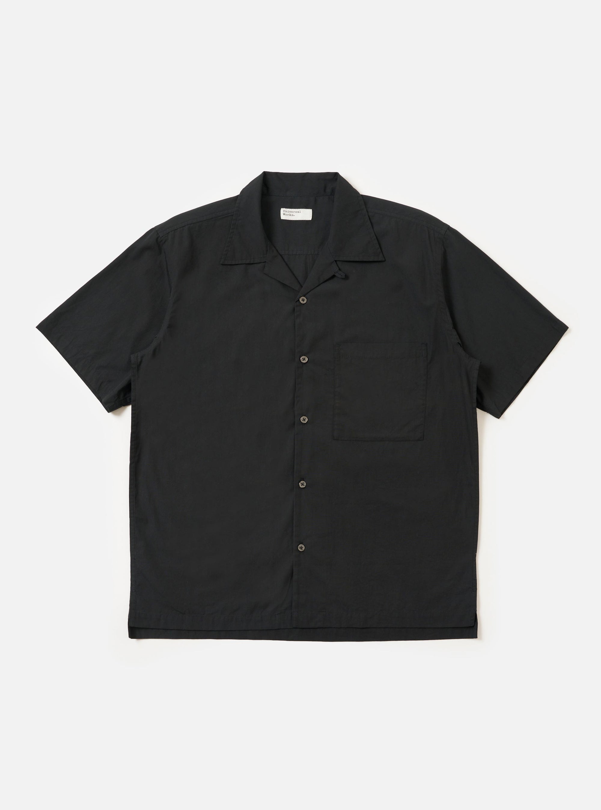 The Black Broadcloth Camp Shirt is shown laid flat against a solid white background. The shirt features a one-piece camp collar, a button-down front, and a single large chest pocket on the left side. The short-sleeve garment is made from a smooth, black broadcloth cotton fabric.