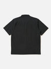 The Black Broadcloth Camp Shirt is shown from the back, laid flat against a plain white background. The image highlights the shirt's back yoke with small pleats and a straight, elongated hem with side splits.