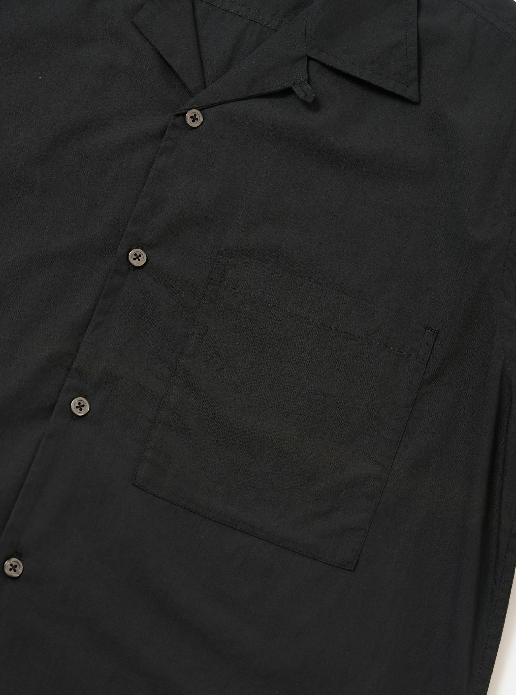 A Black Broadcloth Camp Shirt is displayed flat against a plain white background. The shirt features a classic camp collar, a full button-down front, and short sleeves. The fabric is a smooth black cotton broadcloth.