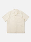 The Ecru Broadcloth Camp Shirt is shown laid flat against a solid white background. The shirt features a relaxed fit, short sleeves, and a classic one-piece camp collar. A single large square chest pocket is visible on the left side, and the front has a tonal button closure.