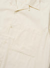The Ecru Broadcloth Camp Shirt is shown from the back, laid flat against a plain white background. The image highlights the horizontal back yoke with two small pleats for added volume and the straight hem with side splits. The short sleeves are laid out to the sides, and