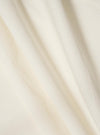 A close-up fabric swatch of the Ecru Broadcloth Camp Shirt displays the fine, smooth weave and off-white color of the broadcloth material. The image focuses on the texture and uniform finish of the cotton fabric.