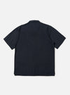 The Navy Broadcloth Camp Shirt is shown from the back, laid flat against a plain white background. The image highlights the back yoke with small pleats and the straight hem with side splits. The short-sleeved garment is made from a navy blue 100% cotton plain weave fabric.