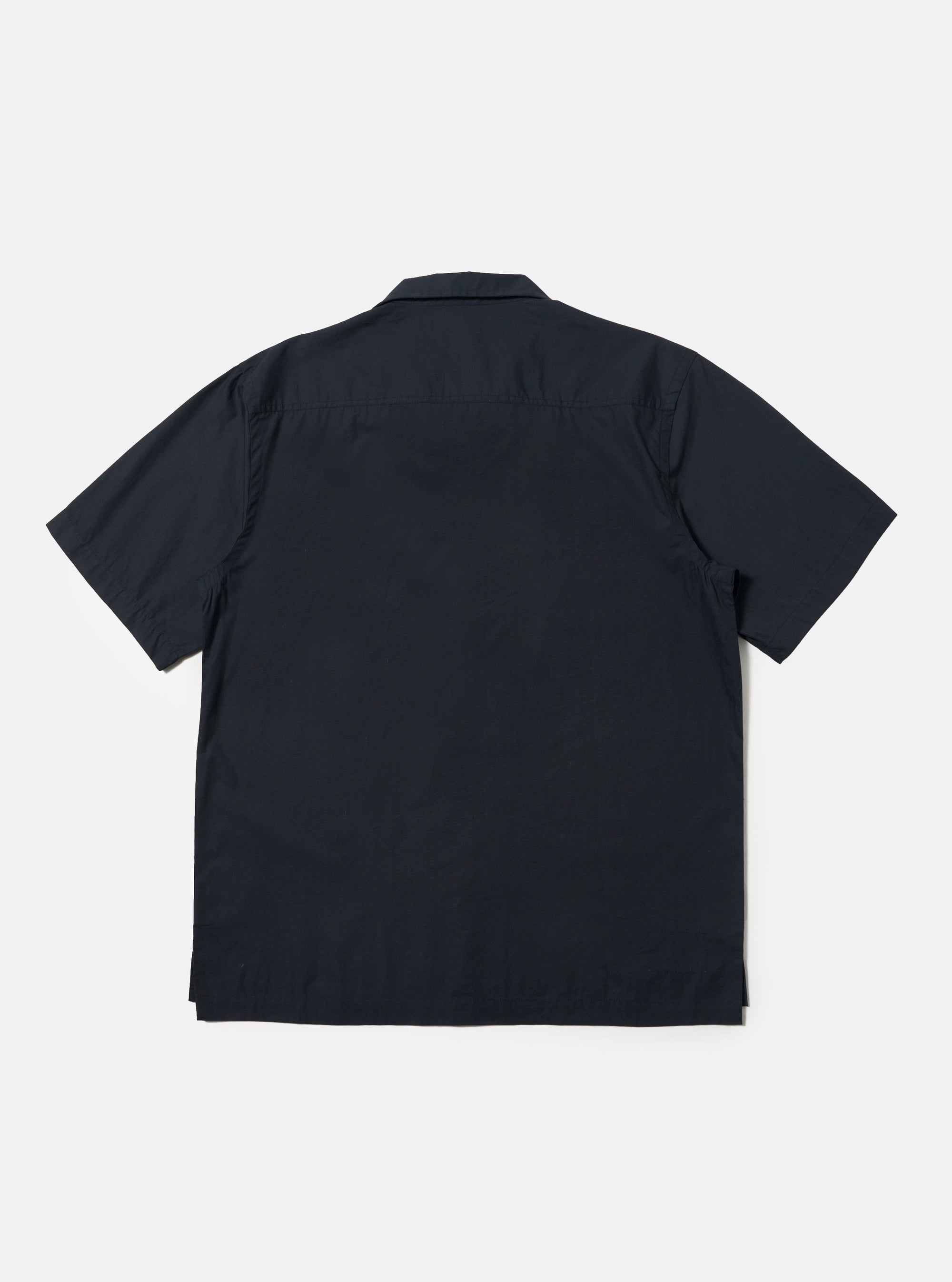 The Navy Broadcloth Camp Shirt is shown from the back, laid flat against a plain white background. The image highlights the back yoke with small pleats and the straight hem with side splits. The short-sleeved garment is made from a navy blue 100% cotton plain weave fabric.