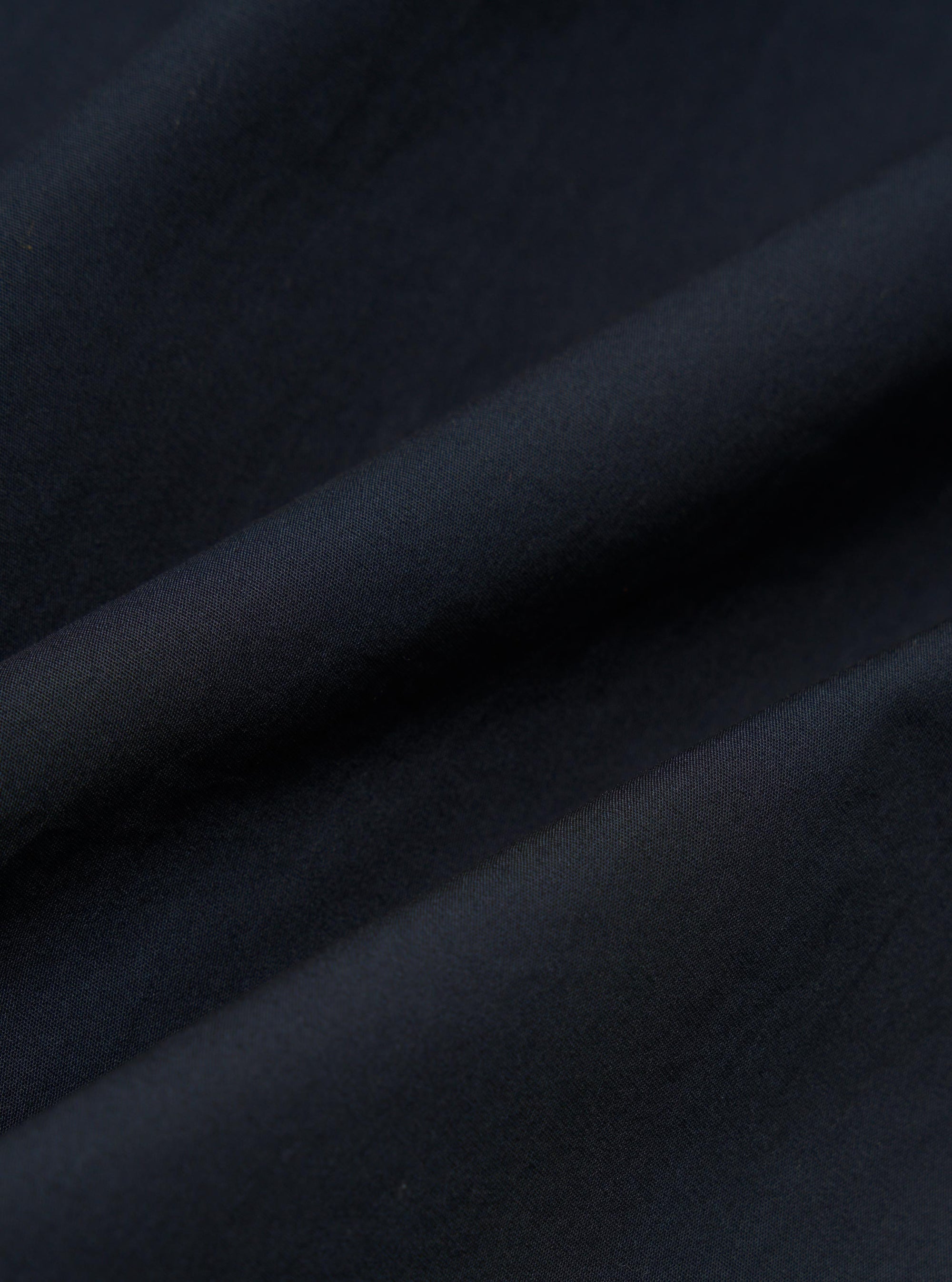 A close-up fabric swatch of the Navy Broadcloth Camp Shirt displays a smooth, tightly woven cotton fabric in a solid navy blue color. The image focuses on the uniform texture and fine weave of the material.