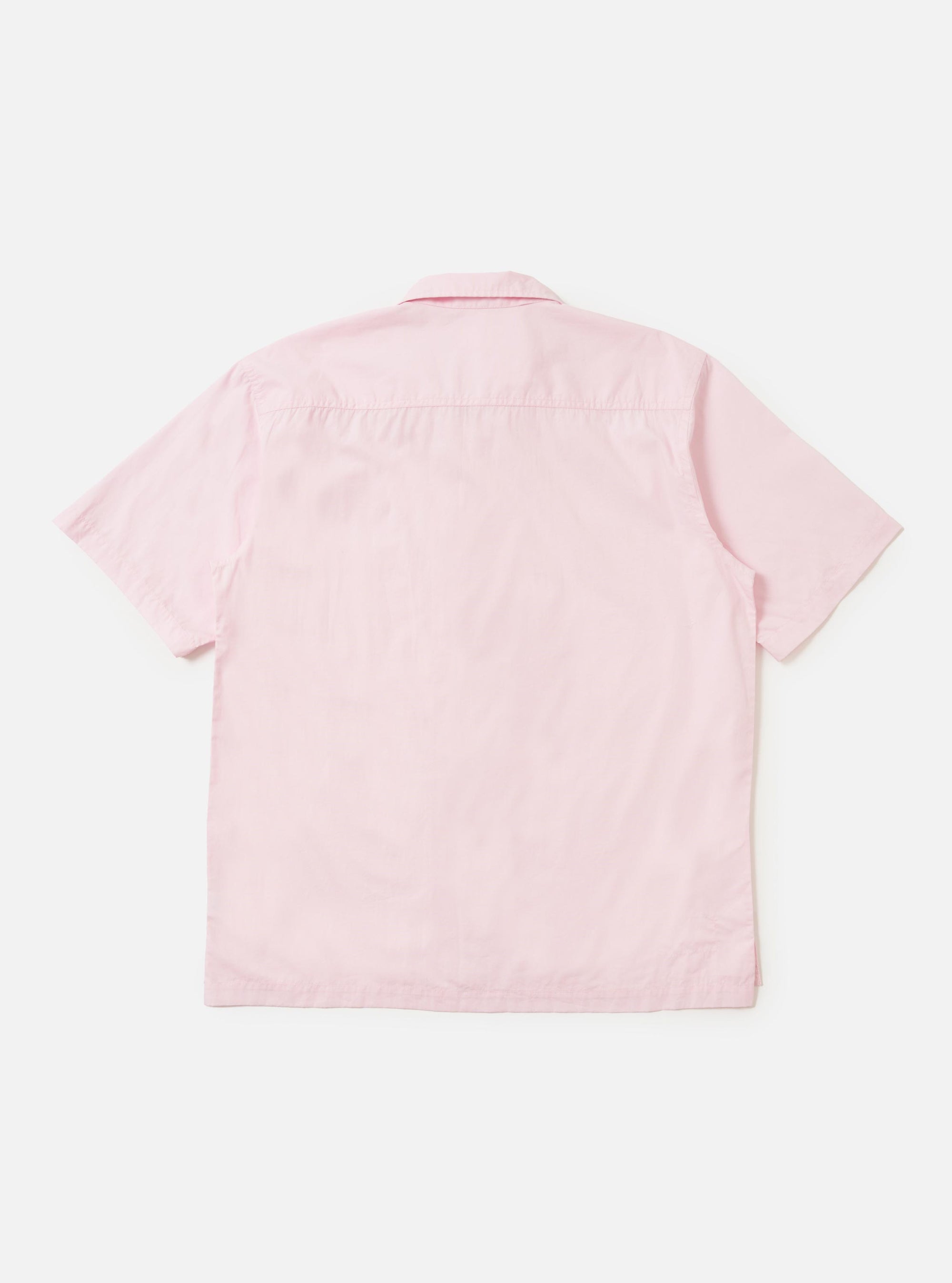 A model is wearing a Pale Pink Broadcloth Camp Shirt against a plain white background. The model is standing with one hand in their pocket, showcasing the loose, relaxed fit of the short-sleeved shirt. Prominent features include the open camp collar, a large chest pocket on the left side, and a straight hem. No mannequin is present in the image.