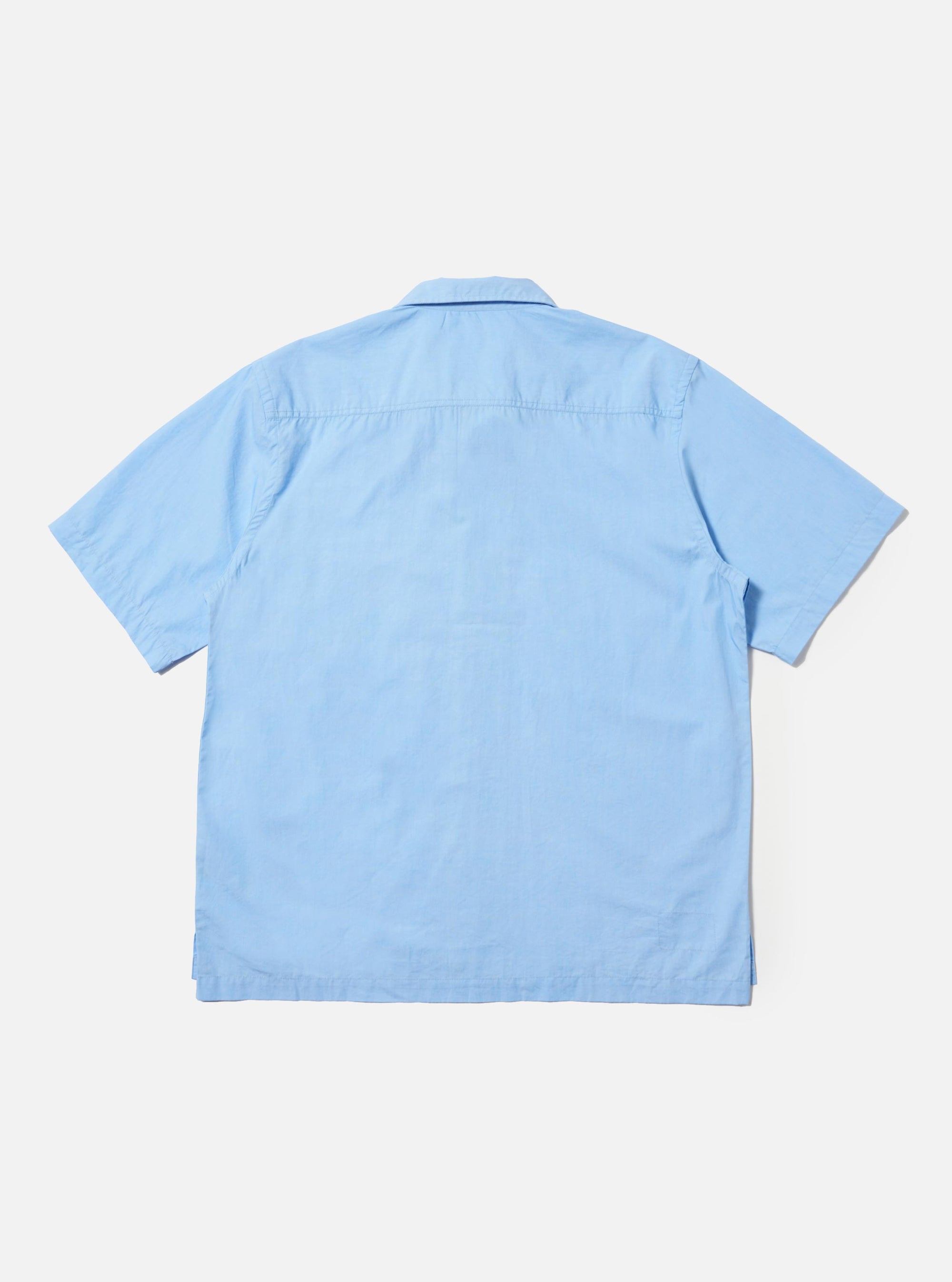 A Pale Blue Broadcloth Camp Shirt is shown from the back, laid flat against a plain white background. The image prominently features the back yoke with small pleats and a straight, even hem.