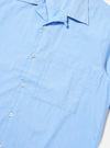 A detail view of the Pale Blue Broadcloth Camp Shirt is shown from the back, laid flat against a solid white background. The image focuses on the upper portion of the garment, specifically highlighting the back yoke and the subtle pleats at the shoulders.