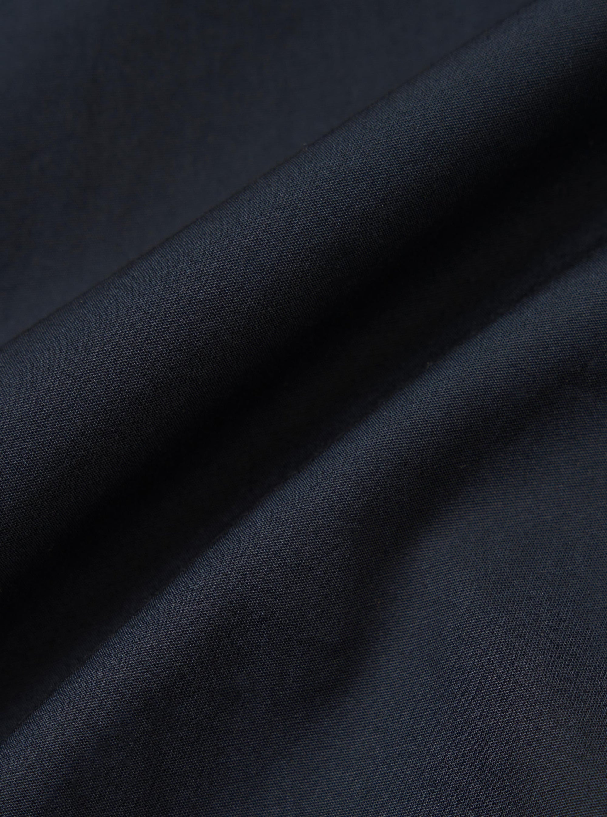 A close-up fabric swatch of the Navy Broadcloth Lucky Shirt shows the smooth, tightly woven texture of the navy blue cotton material. The image focuses on the uniform color and fine grain of the broadcloth fabric.