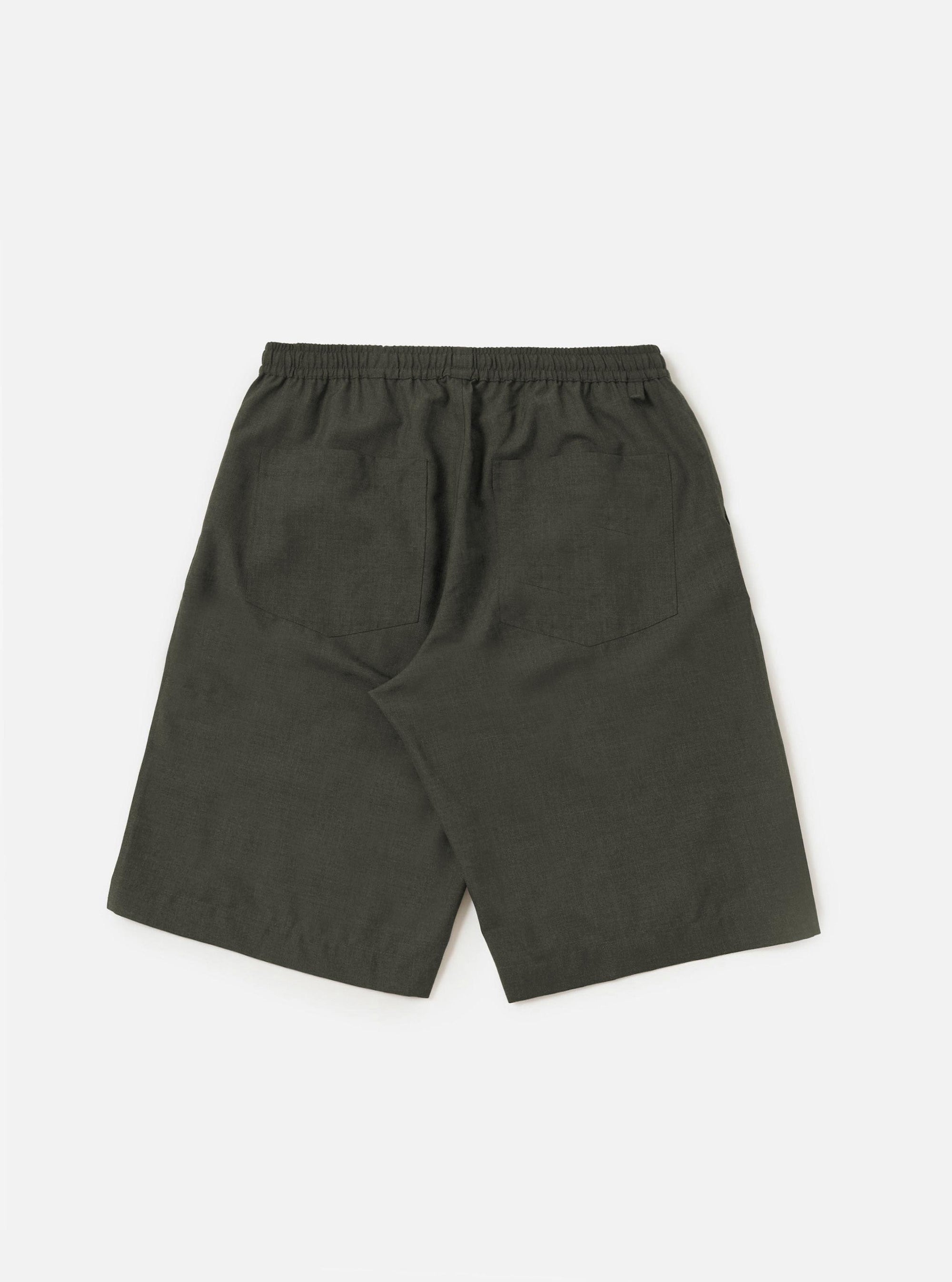 A model is shown from the waist down wearing the Olive Marl Tropical Suiting Vacation Short against a plain white background. The shorts feature a relaxed, knee-length fit and a drawstring waist, highlighting the textured olive marl fabric. The model's hands are placed in the side seam pockets.