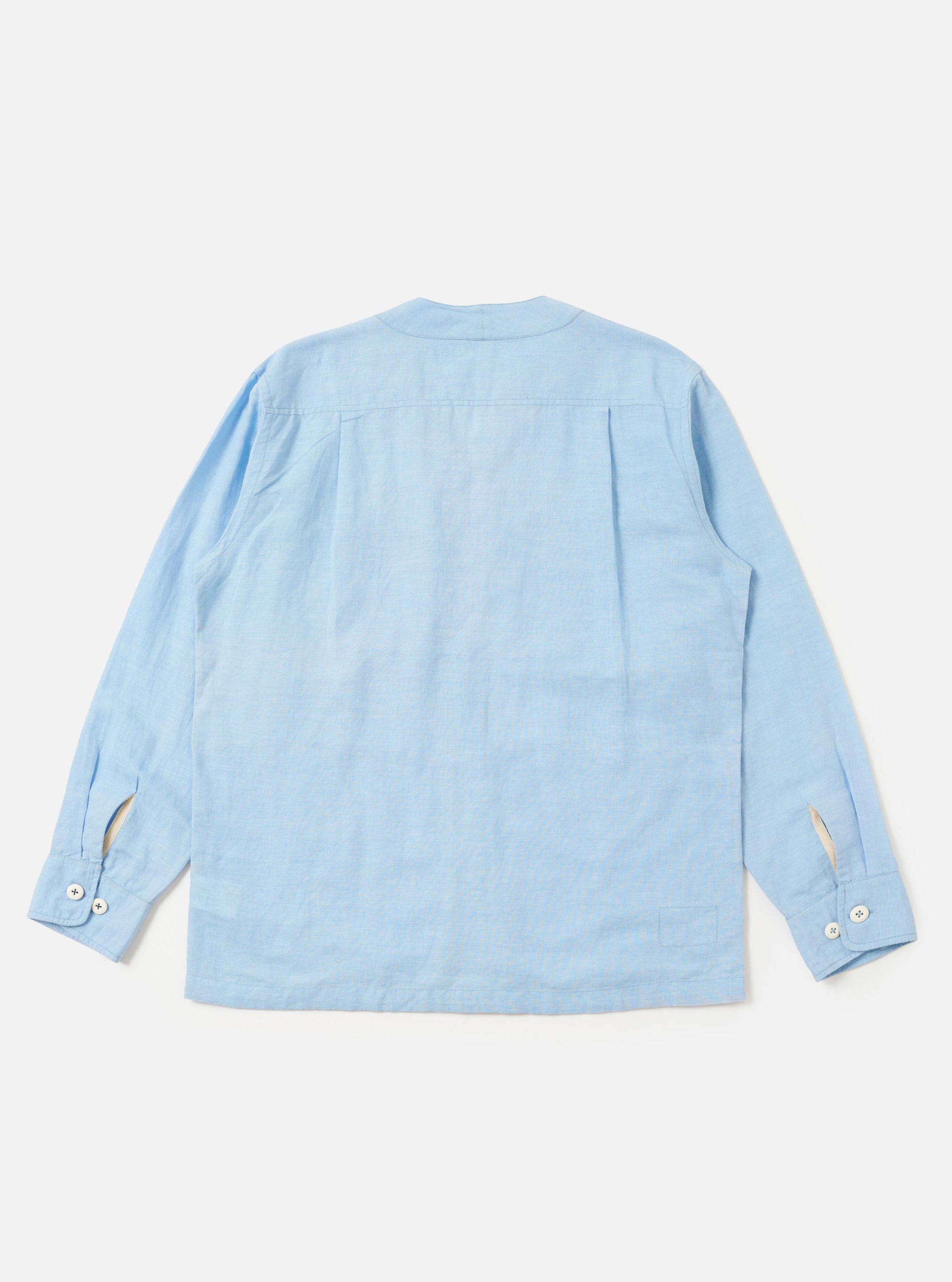 A model wears the Pale Blue Linen Cotton Shirting Parachute Shirt, shown from the front against a plain white background. The shirt features a relaxed fit, a classic collar, a full button-down front, and two large chest pockets. The model is standing with their hands by their sides, and the light blue fabric exhibits a subtle, natural linen texture.