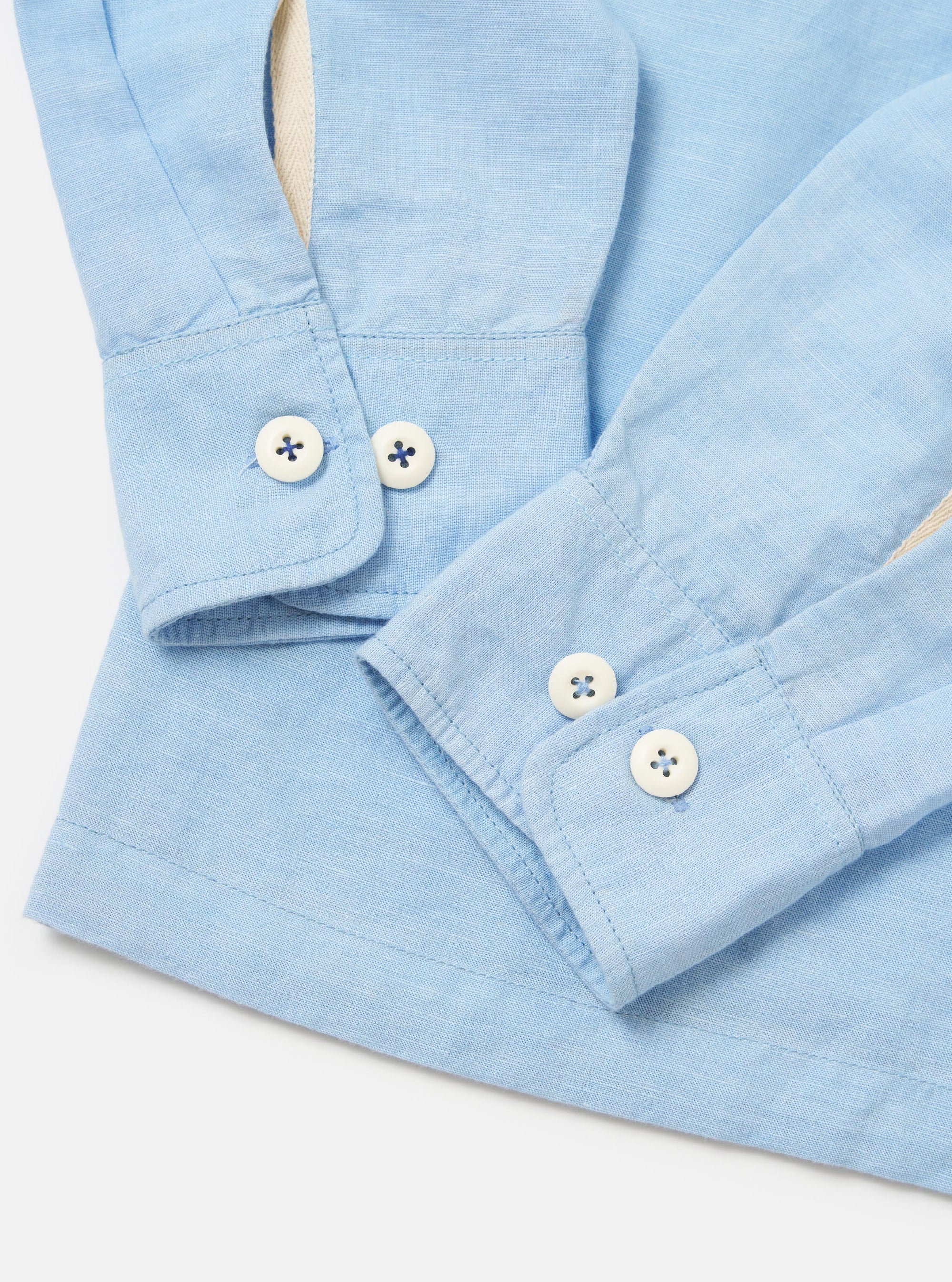 A model is wearing the Pale Blue Linen Cotton Shirting Parachute Shirt, shown from a rear side angle against a plain white background. The shirt features a relaxed fit with long sleeves, a pointed collar, and a straight hem. The light blue fabric has a subtle textured weave. No other items are prominent in the image.