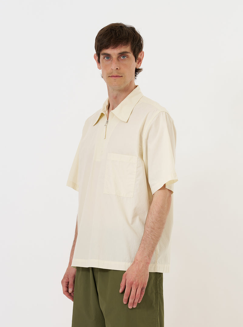 A model is wearing the Ecru Broadcloth Ewan Shirt against a plain white background. The shirt is a pullover style featuring a quarter-zip front and a classic collar. The model is shown from the chest up, highlighting the crisp ecru cotton fabric and the functional zip detail. No mannequin is present in the image.