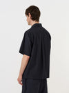 A model is wearing the Navy Broadcloth Ewan Shirt, shown from the back against a plain white background. The shirt is a navy blue pullover style with a zip detail at the neck, featuring a classic collar and a straight hem. The model is standing, and the image highlights the clean construction and smooth texture of the broadcloth fabric. No mannequin is present in the image.