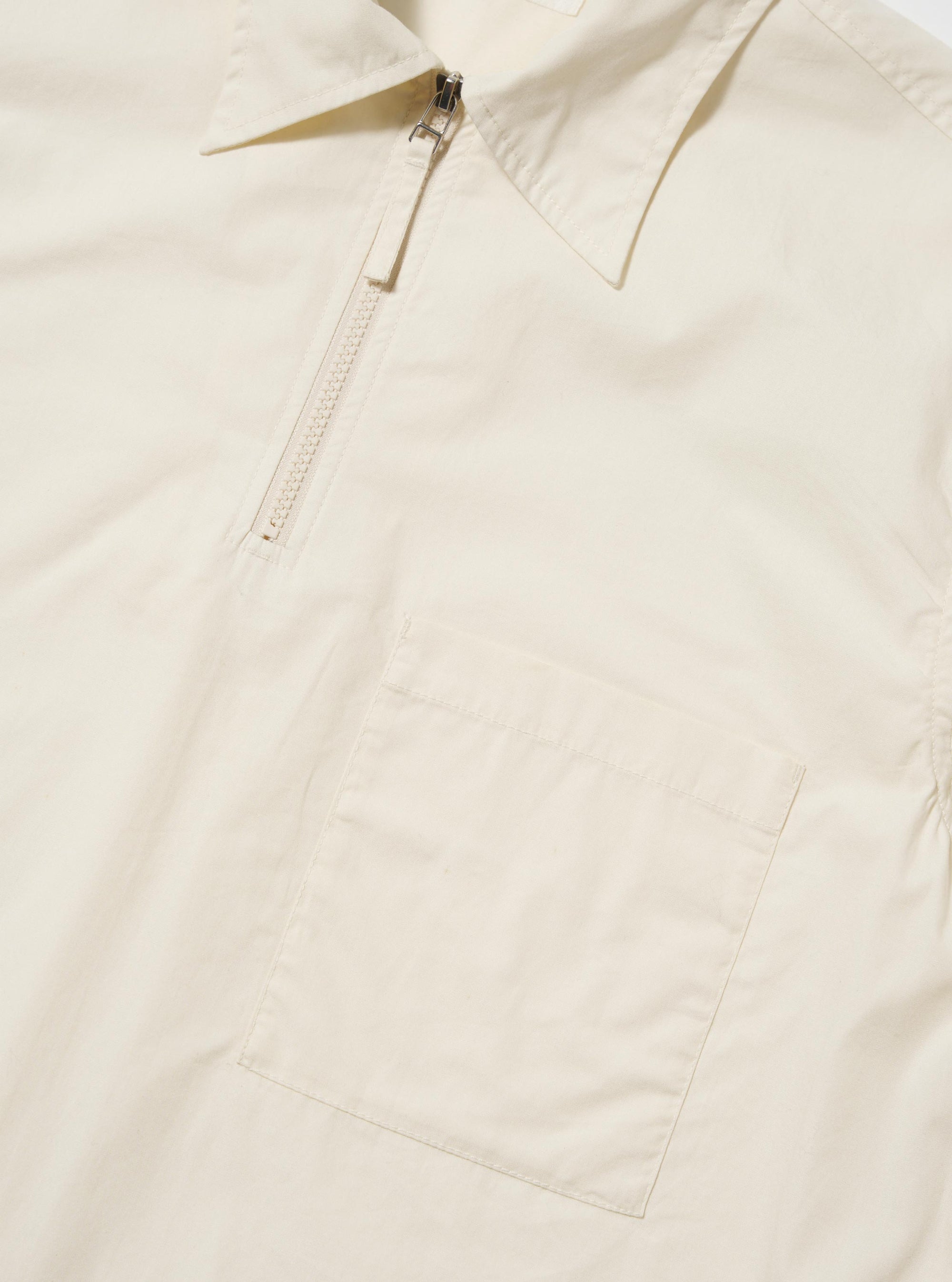 The Ecru Broadcloth Ewan Shirt is shown from the back, laid flat against a plain white background. The image highlights the shirt's long sleeves, straight hem, and horizontal back yoke. The garment is made from a smooth, off-white broadcloth material.
