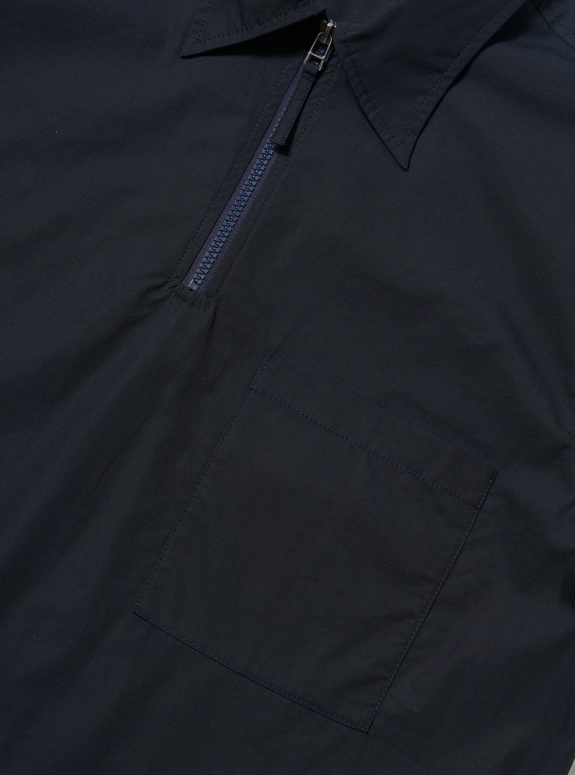 The Navy Broadcloth Ewan Shirt is shown from the back, displayed flat against a plain white background. The image highlights the short-sleeve silhouette, a straight hem with small side splits, and a horizontal yoke across the shoulders with a central box pleat.