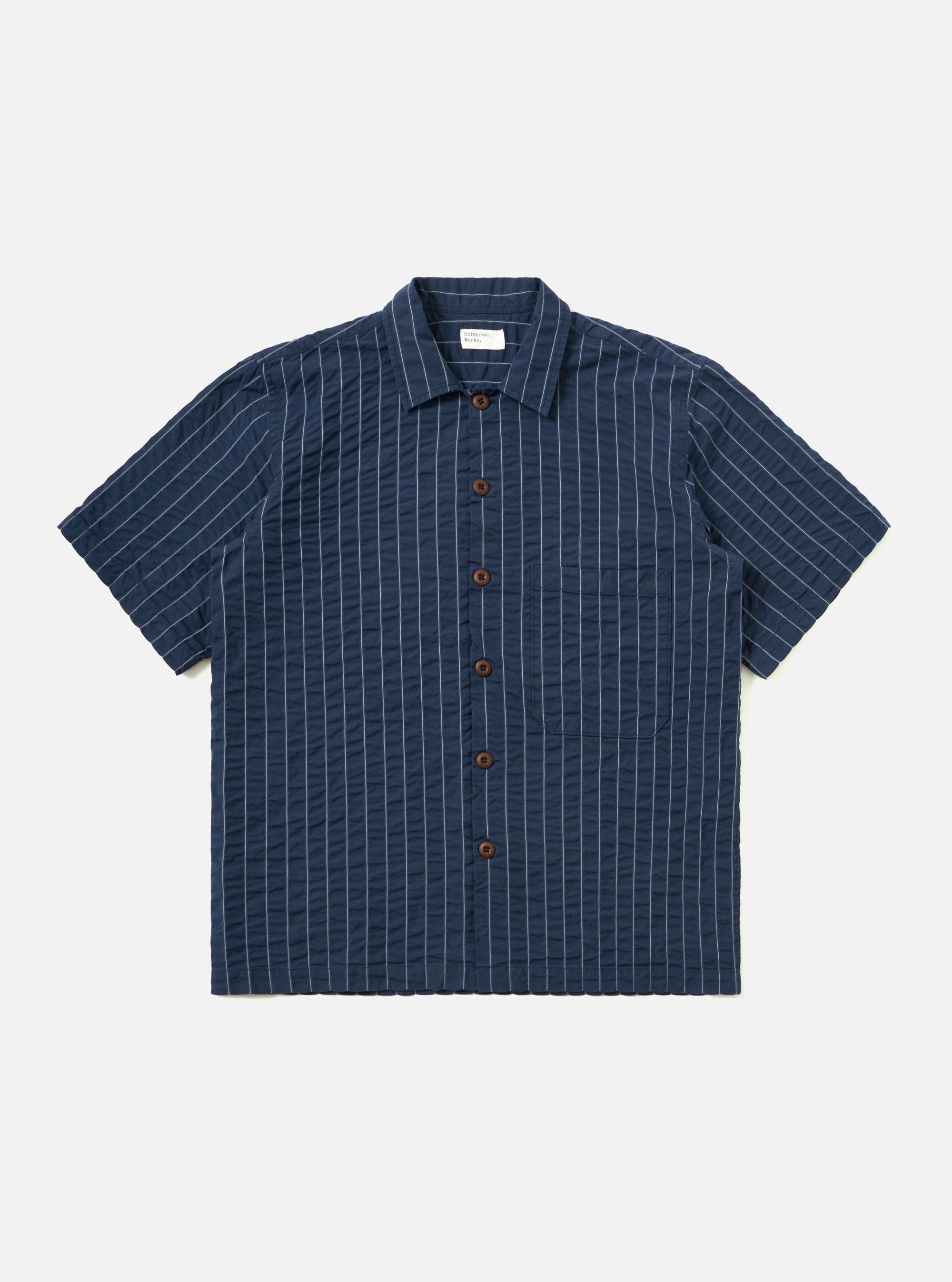 A Navy Chester Stripe S/S Fatigue Shirt is shown laid flat against a solid white background. The garment features a navy blue and white vertical stripe pattern, a classic pointed collar, a full button-down front, and two large chest pockets. The short sleeves are visible, and