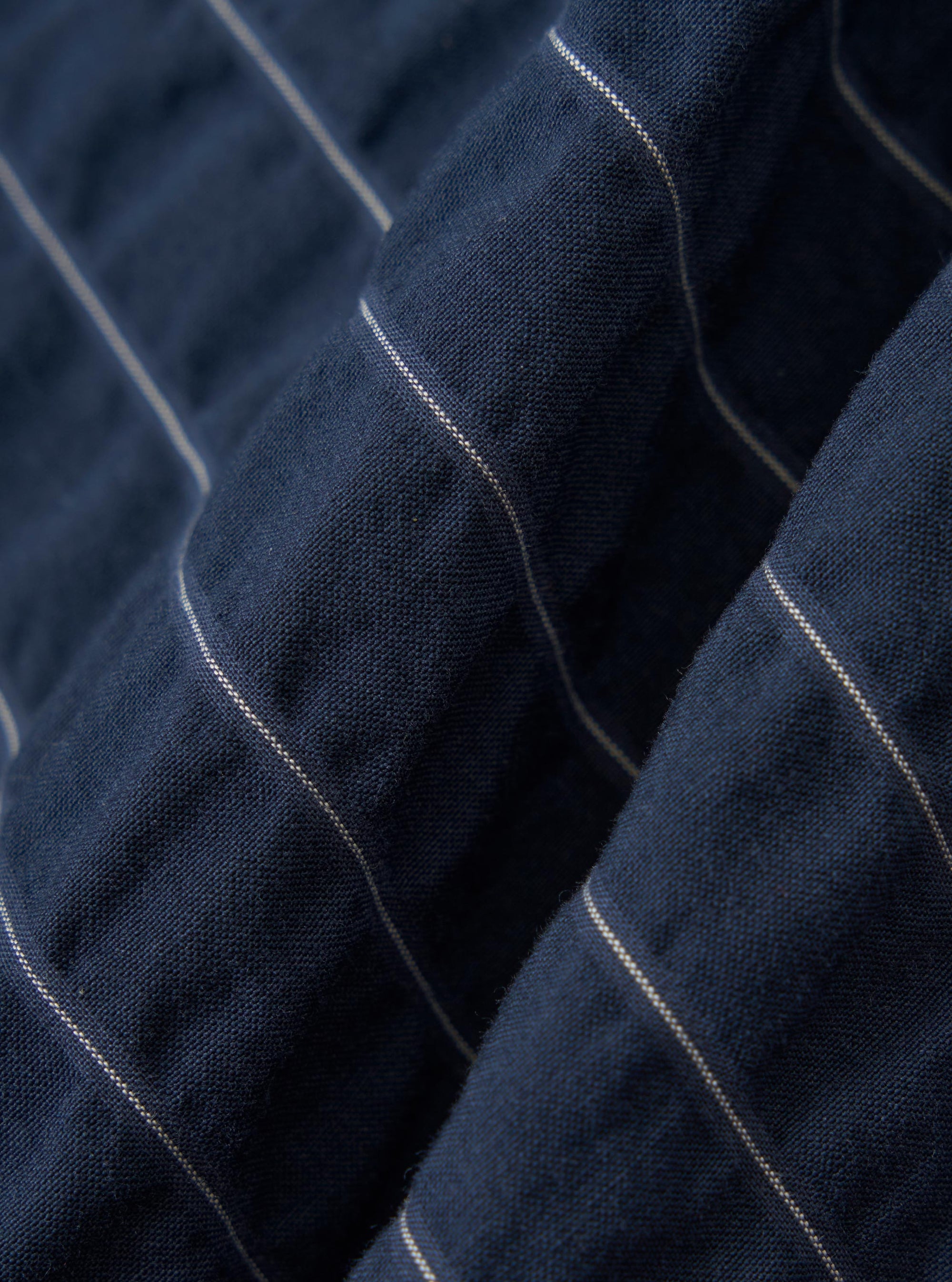 A close-up fabric swatch of the Navy Chester Stripe S/S Fatigue Shirt shows a detailed view of the navy and blue chester stripe pattern. The image focuses on the texture and weave of the cotton fabric.