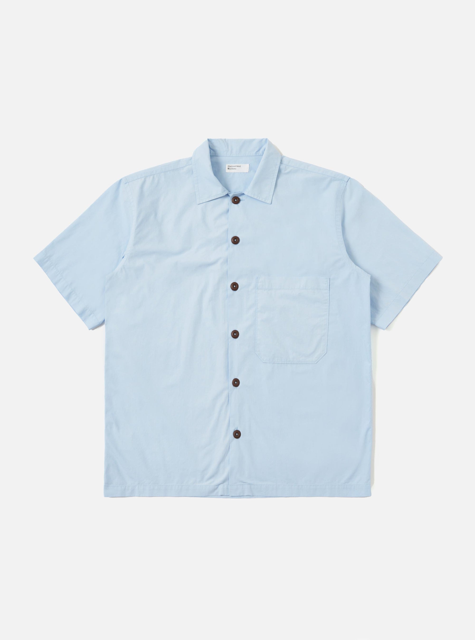 A Sky Blue Paper Touch Cotton S/S Fatigue Shirt is shown laid flat against a plain white background. The short-sleeved overshirt features a classic pointed collar, a full button-down front with tonal buttons, and a single large patch pocket on the left chest. The fabric has a smooth, crisp texture and a straight hem.