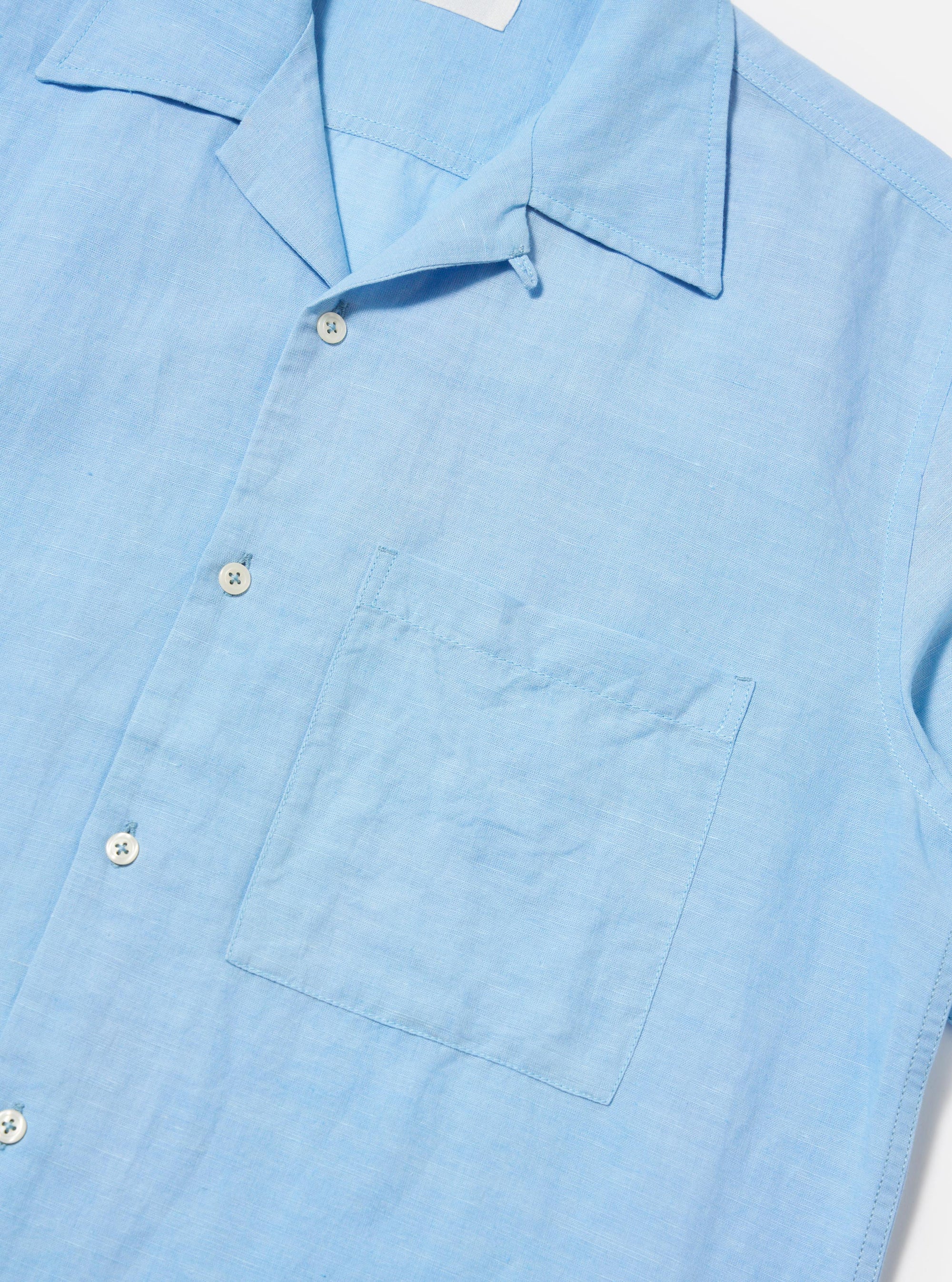 The Pale Blue Linen Cotton Shirting Camp Shirt is shown from the back, worn by a model standing against a plain white background. The shirt features a relaxed fit, a straight hem, and short sleeves. The model is also wearing dark trousers, though only the upper portion is visible.