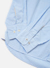 The Sky/White Classic Nipon Stripe Lazy Day Shirt is shown from the back, laid flat against a solid white background. The garment features thin light blue and white vertical stripes. Key details include a horizontal back yoke and a central box pleat that adds volume to the relaxed silhouette.