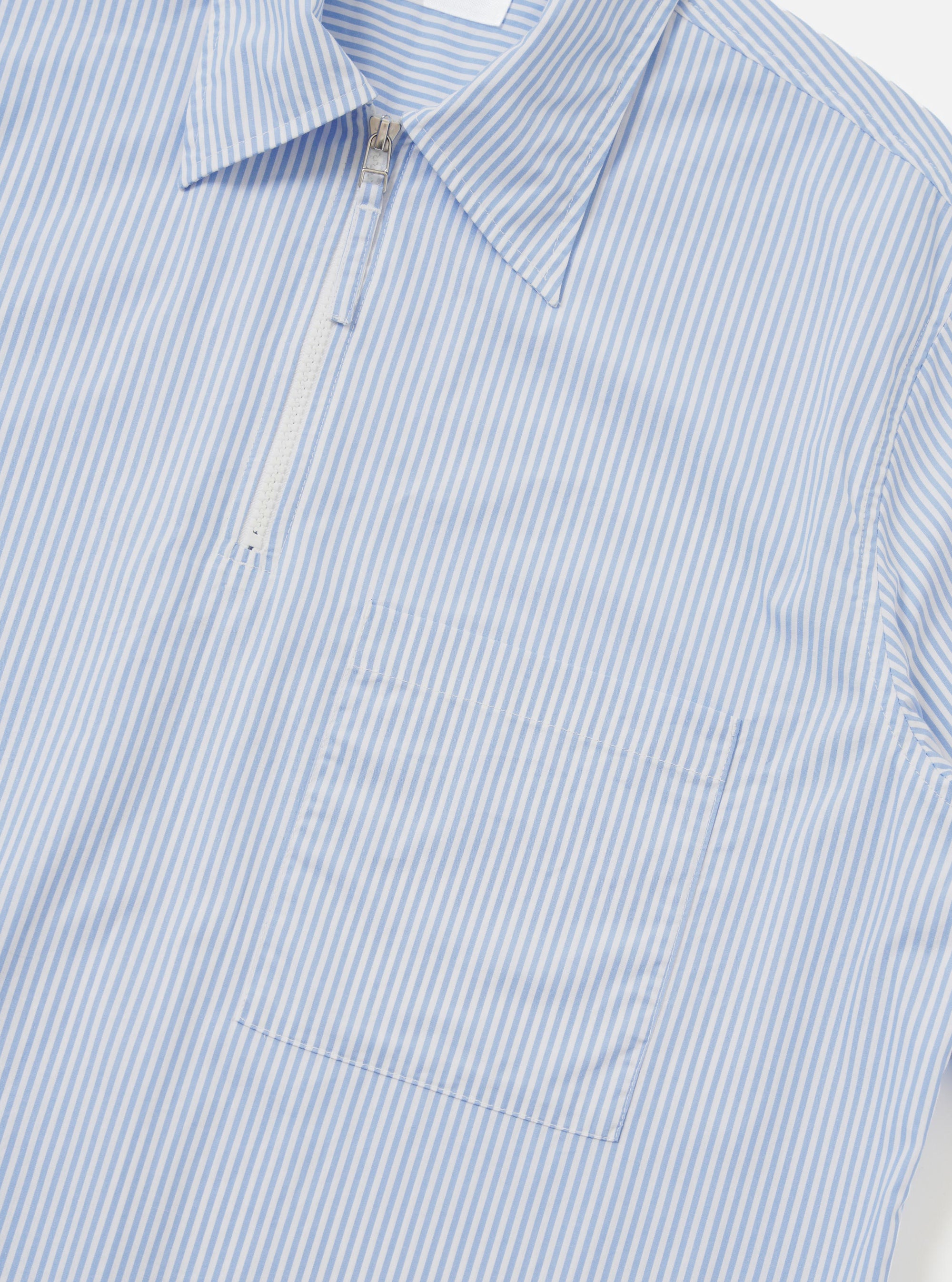 A rear view of the Sky/White Classic Nipon Stripe Ewan Shirt is shown laid flat against a plain white background. The image highlights the blue and white vertical stripes, a straight hem, and a simple horizontal yoke across the shoulders.