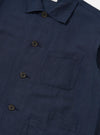 A model stands against a plain white background wearing the Navy Linen Cotton Shirting Bakers Overshirt over a white t-shirt. The navy overshirt features a classic collar, button-down front, and three large patch pockets on the front. The fabric has a visible linen texture, and the model has their hands by their sides.