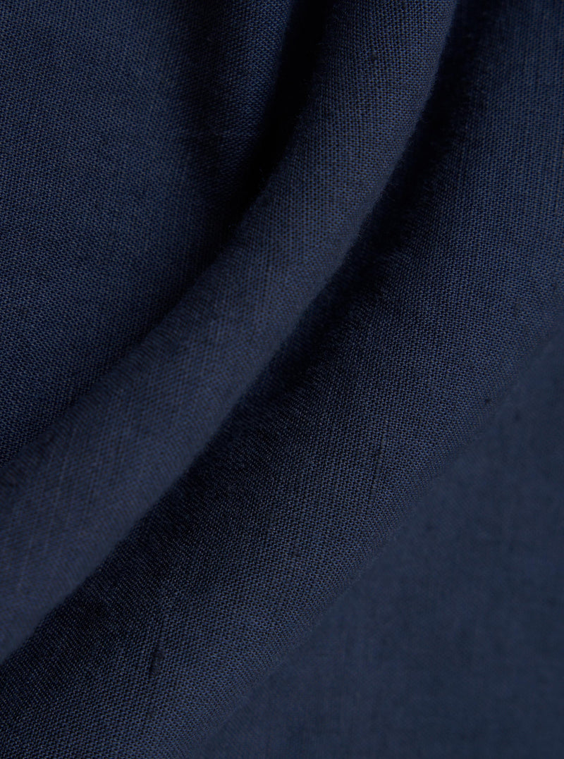A detailed, close-up fabric swatch of the Navy Linen Cotton Shirting Bakers Overshirt displays a dark navy blue textile with a visible, textured weave pattern. The fabric is shown flat and fills the frame.