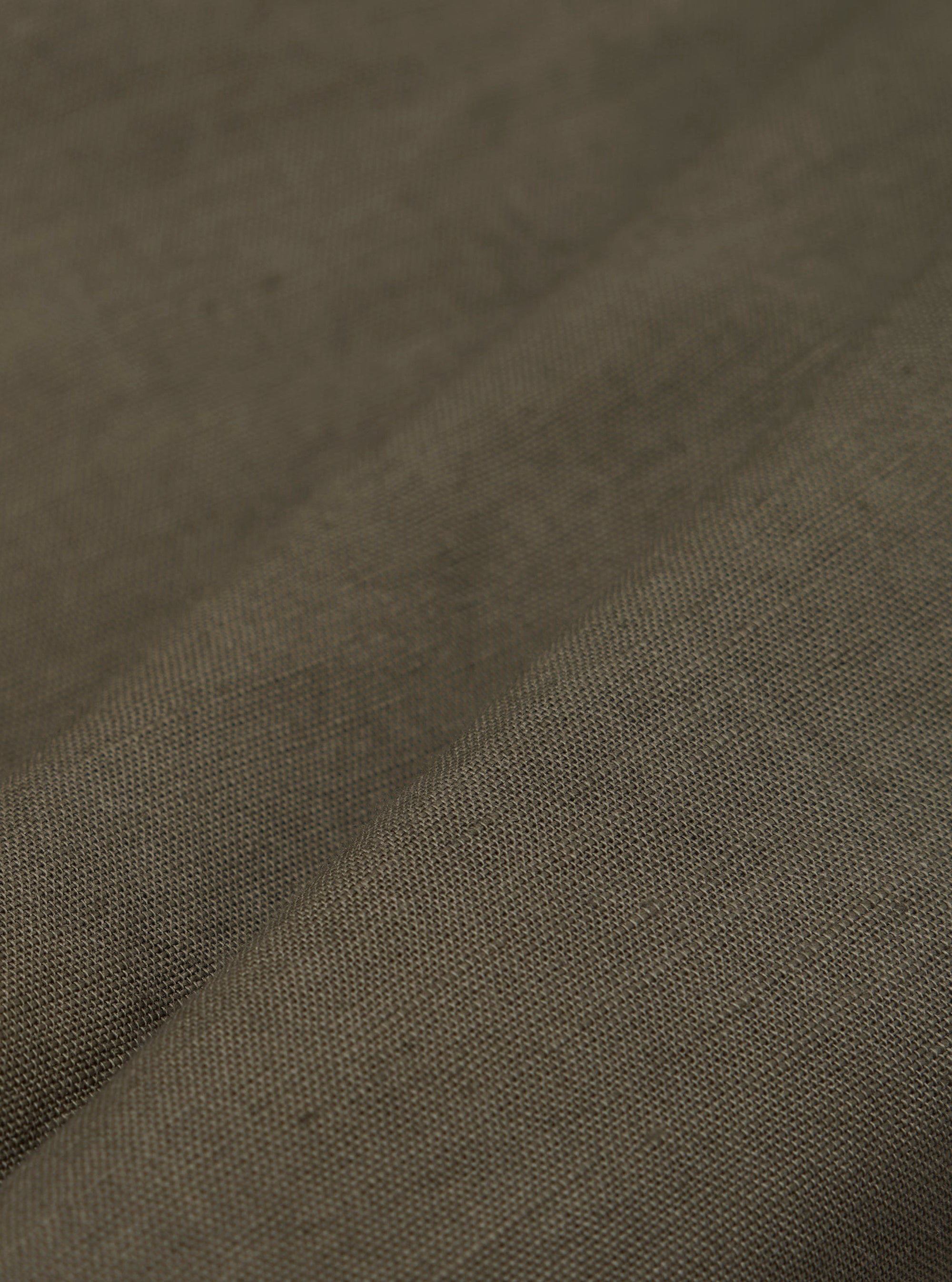 A detailed, close-up fabric swatch of the olive green linen-cotton shirting material used for the Bakers Overshirt. The image highlights the textured weave and solid color of the fabric.
