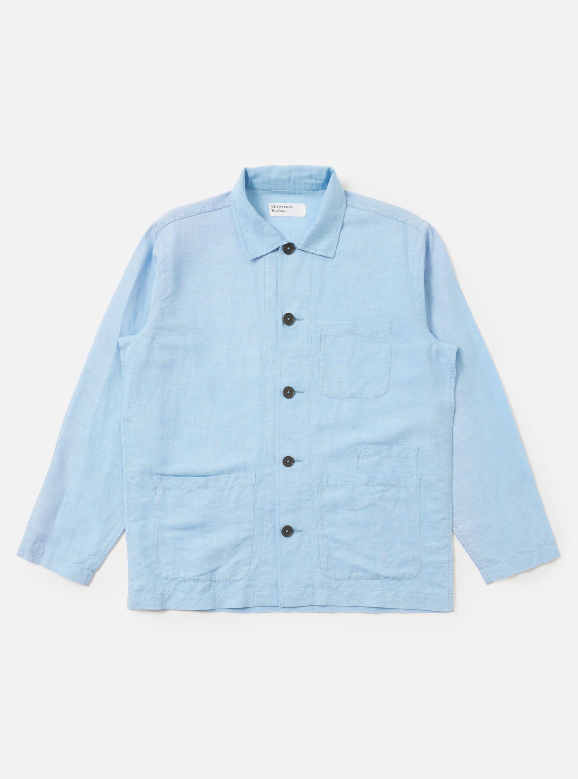 A Pale Blue Linen Cotton Shirting Bakers Overshirt is shown laid flat against a solid white background. The garment features a classic pointed collar, a full button-down front, one asymmetric chest pocket, and two large patch pockets at the waist. The light blue fabric has a subtle, textured appearance.