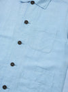 The Pale Blue Linen Cotton Shirting Bakers Overshirt is shown from the back, laid flat against a plain white background. The image highlights the straight hem, the simple one-piece collar, and the lightweight, textured linen-cotton fabric.