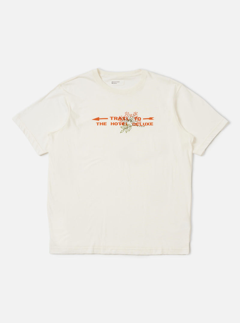The Ecru Single Jersey Trail Trail To Hotel Delux Tee is shown laid flat against a solid white background. The short-sleeved t-shirt features a classic ribbed crew neck and a small graphic print on the left chest.