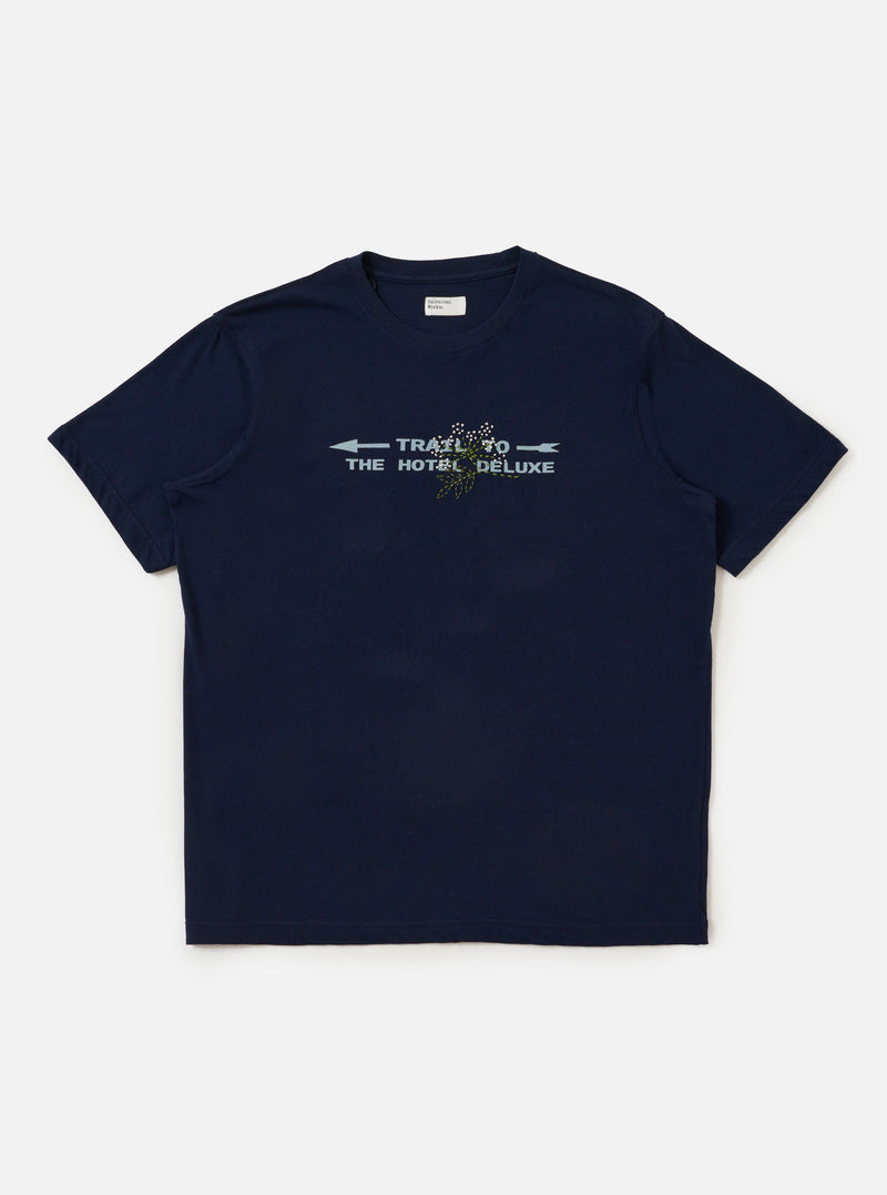 The Navy Single Jersey Trail Trail To Hotel Delux Tee is shown laid flat against a solid white background. The navy blue short-sleeved T-shirt features a classic crew neck and a prominent graphic print on the chest consisting of white text and a circular emblem.