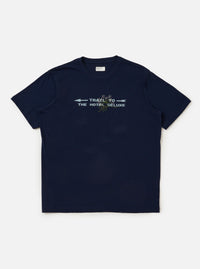 The Navy Single Jersey Trail Trail To Hotel Delux Tee is shown laid flat against a solid white background. The navy blue short-sleeved T-shirt features a classic crew neck and a prominent graphic print on the chest consisting of white text and a circular emblem.
