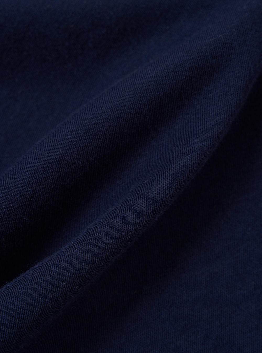 A close-up fabric swatch of the Navy Single Jersey Trail Trail To Hotel Delux Tee shows a detailed view of the navy blue cotton material. The image highlights the soft, knitted texture of the single jersey trail fabric.