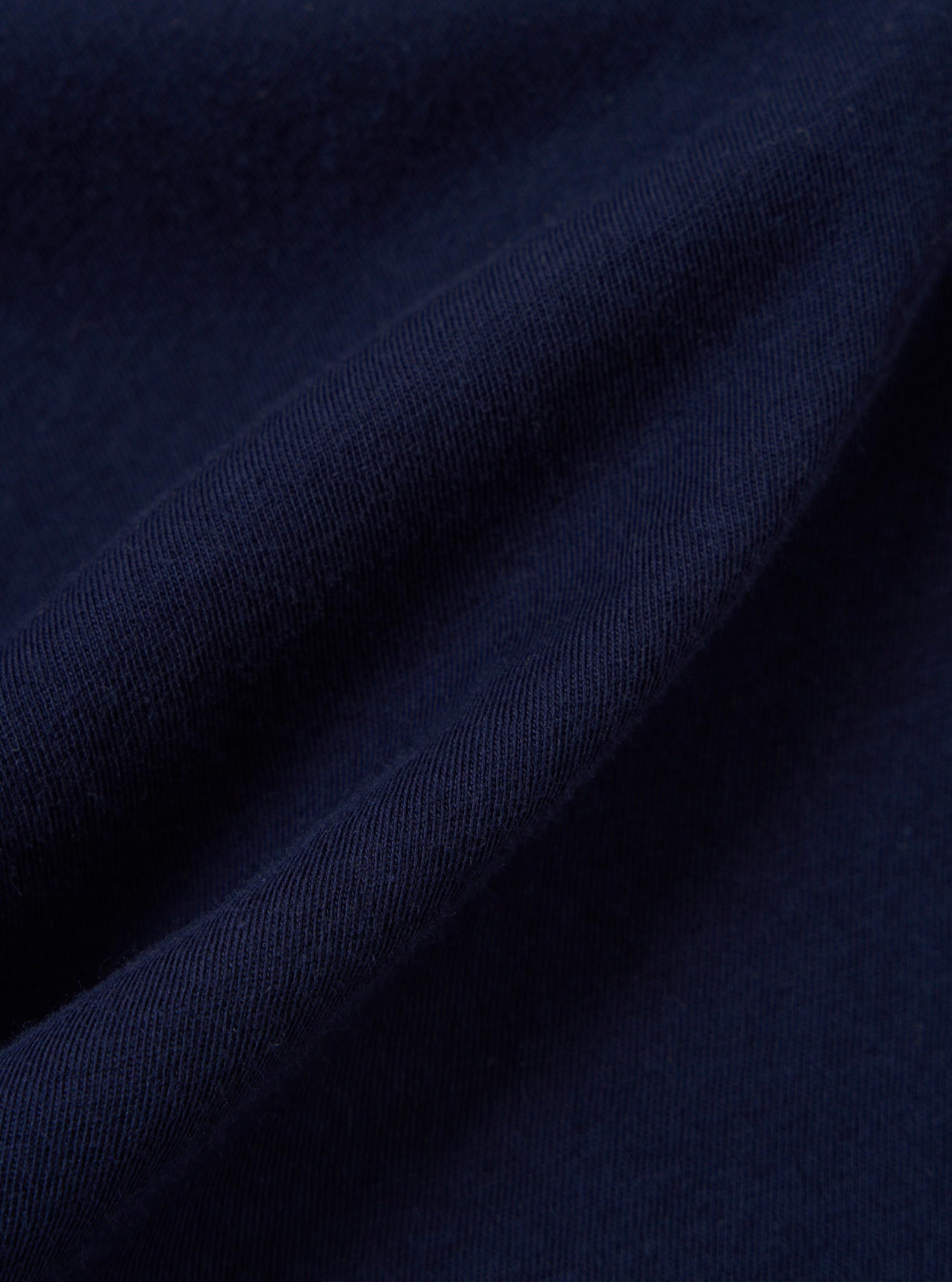 A close-up fabric swatch of the Navy Single Jersey Trail Trail To Hotel Delux Tee shows a detailed view of the navy blue cotton material. The image highlights the soft, knitted texture of the single jersey trail fabric.