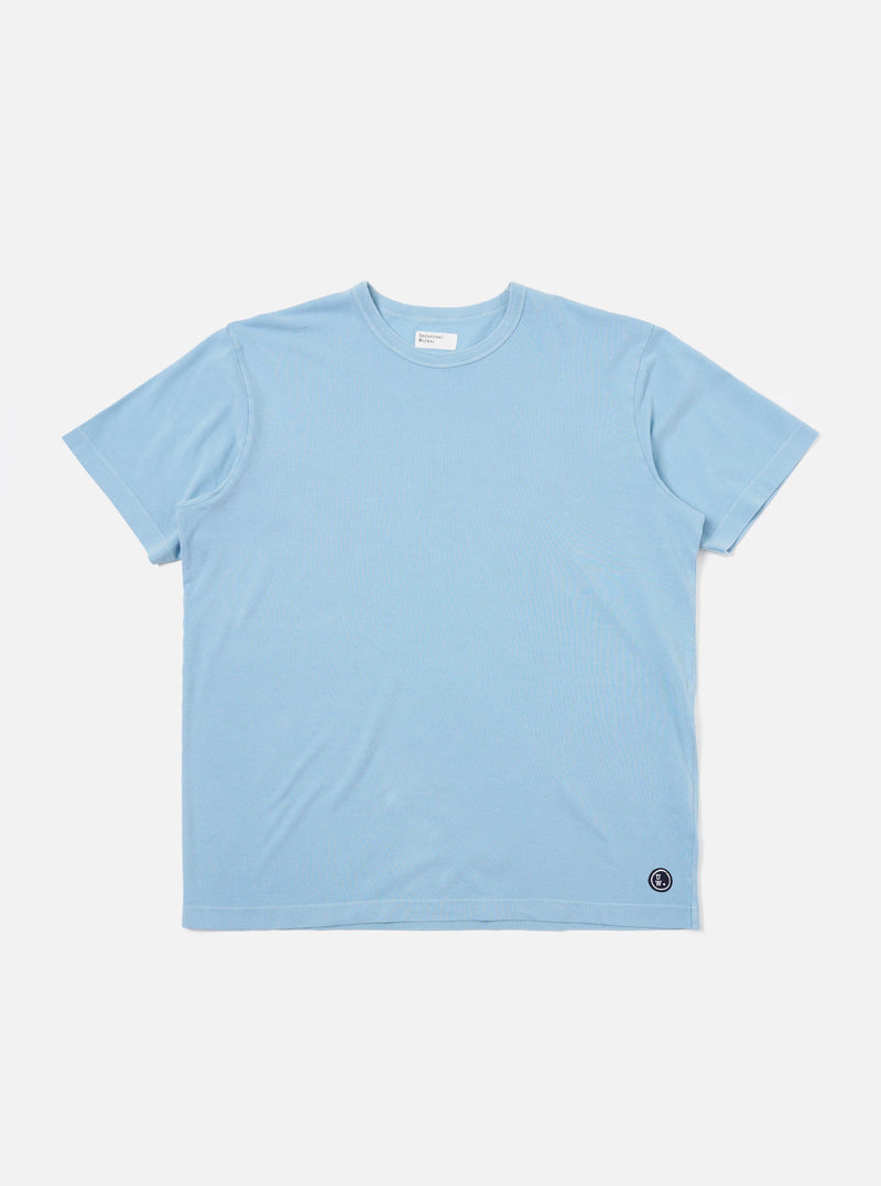 The Pale Blue Piquet Core Tee is shown laid flat against a plain white background. The short-sleeve t-shirt features a classic crew neck with a self-bound collar and a clean, regular-fit silhouette.