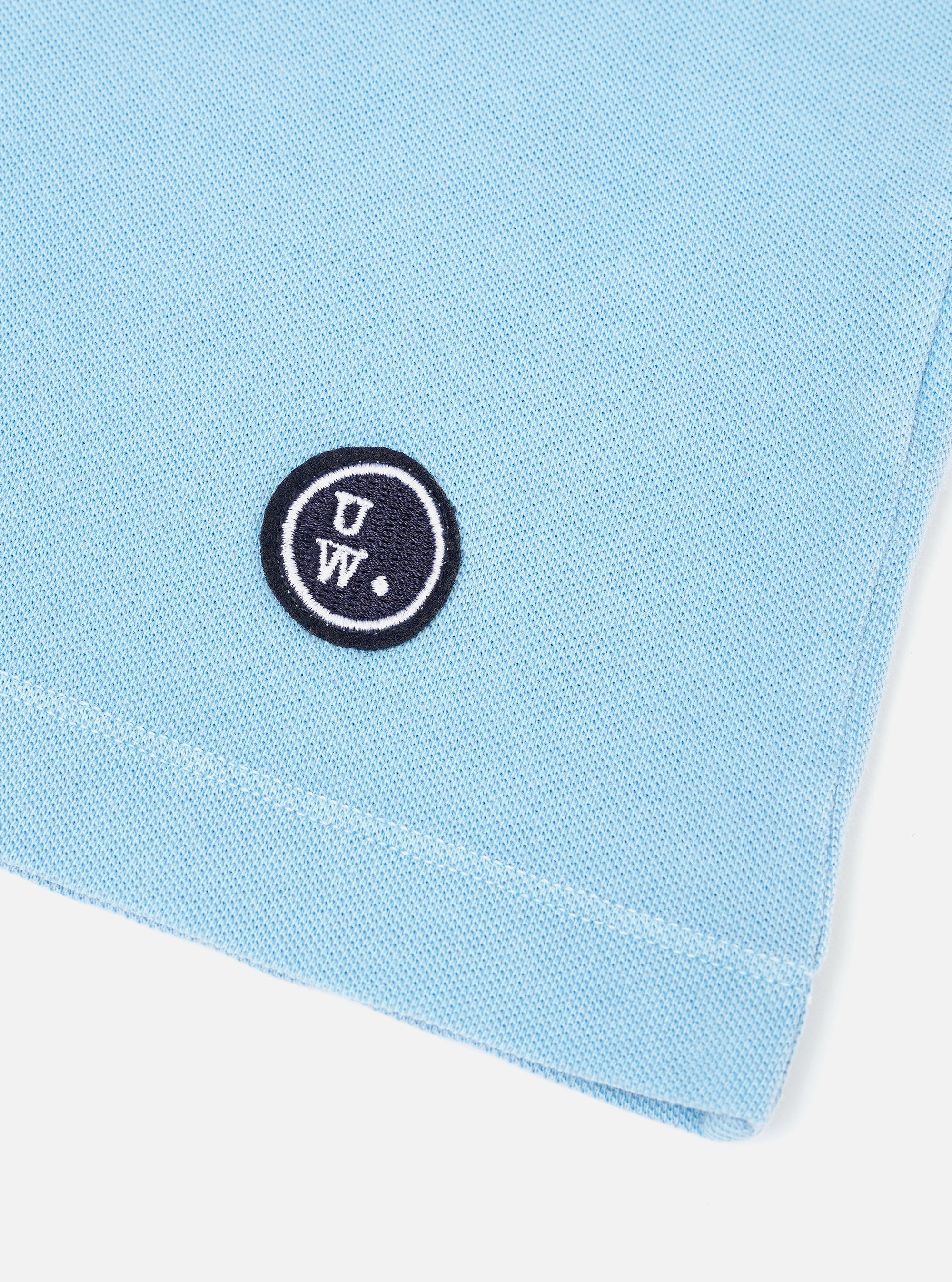 The Pale Blue Piquet Core Tee is shown from the back, laid flat against a plain white background. The image highlights the short sleeves, straight hem, and the textured piquet cotton fabric.