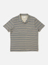 A Grey OS Stripe Jersey Vacation Polo is shown laid flat against a solid white background. The shirt features horizontal light grey and charcoal stripes with an irregular, hand-painted character. It has a relaxed open neck with a single-piece collar, a short front placket, a single patch chest pocket, and a straight hem.