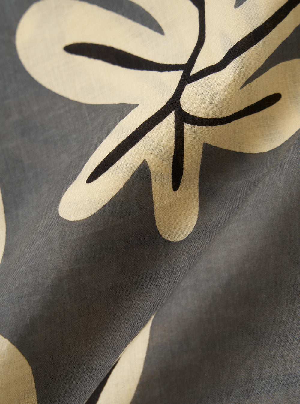 A close-up fabric swatch of the Grey Baja Print Road Shirt showcases a detailed, large-scale botanical motif in dark grey and white against a neutral grey background. The image highlights the intricate printed pattern and the fine texture of the 100% cotton material.