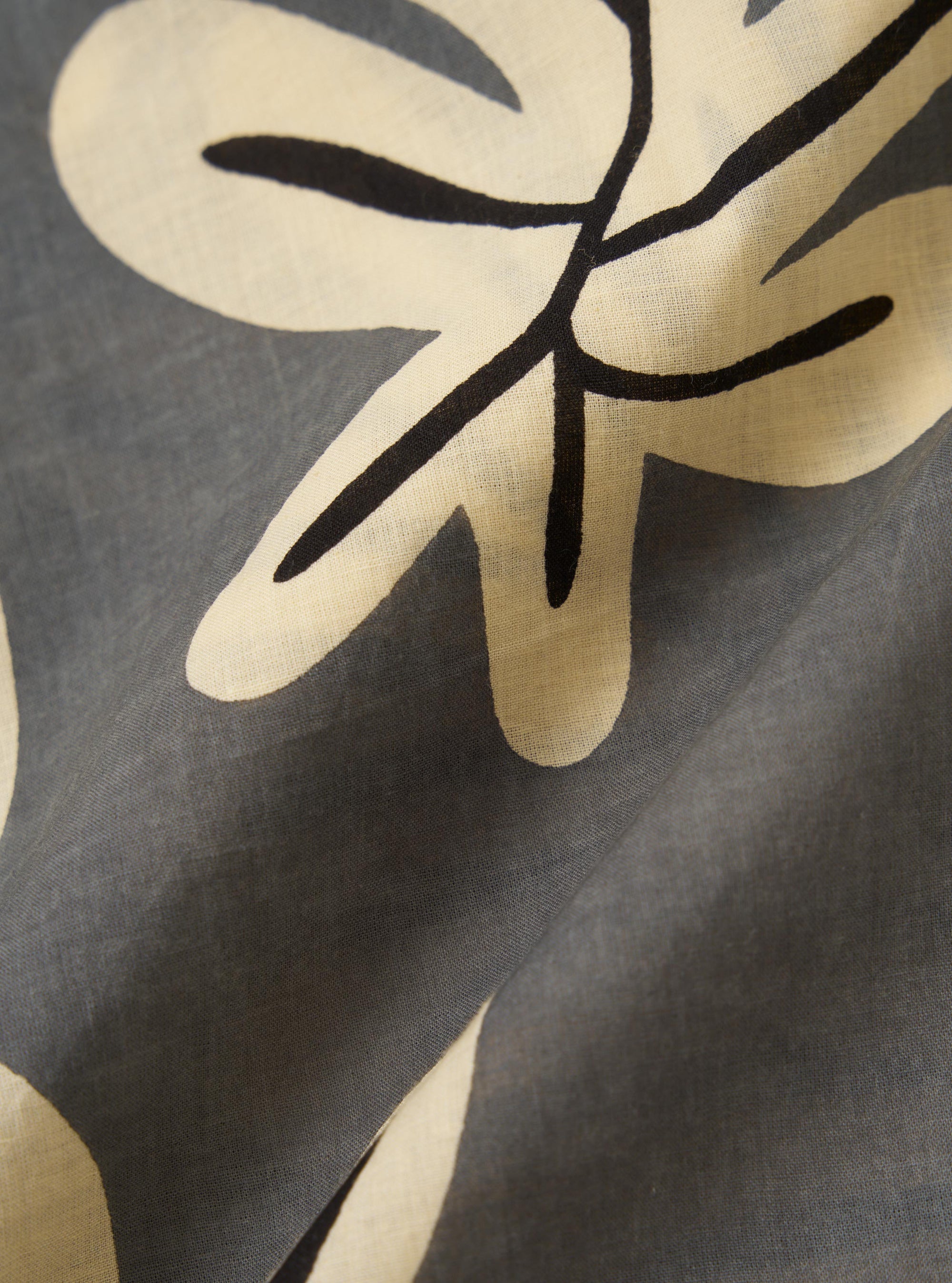 A close-up fabric swatch of the Grey Baja Print Road Shirt showcases a detailed, large-scale botanical motif in dark grey and white against a neutral grey background. The image highlights the intricate printed pattern and the fine texture of the 100% cotton material.