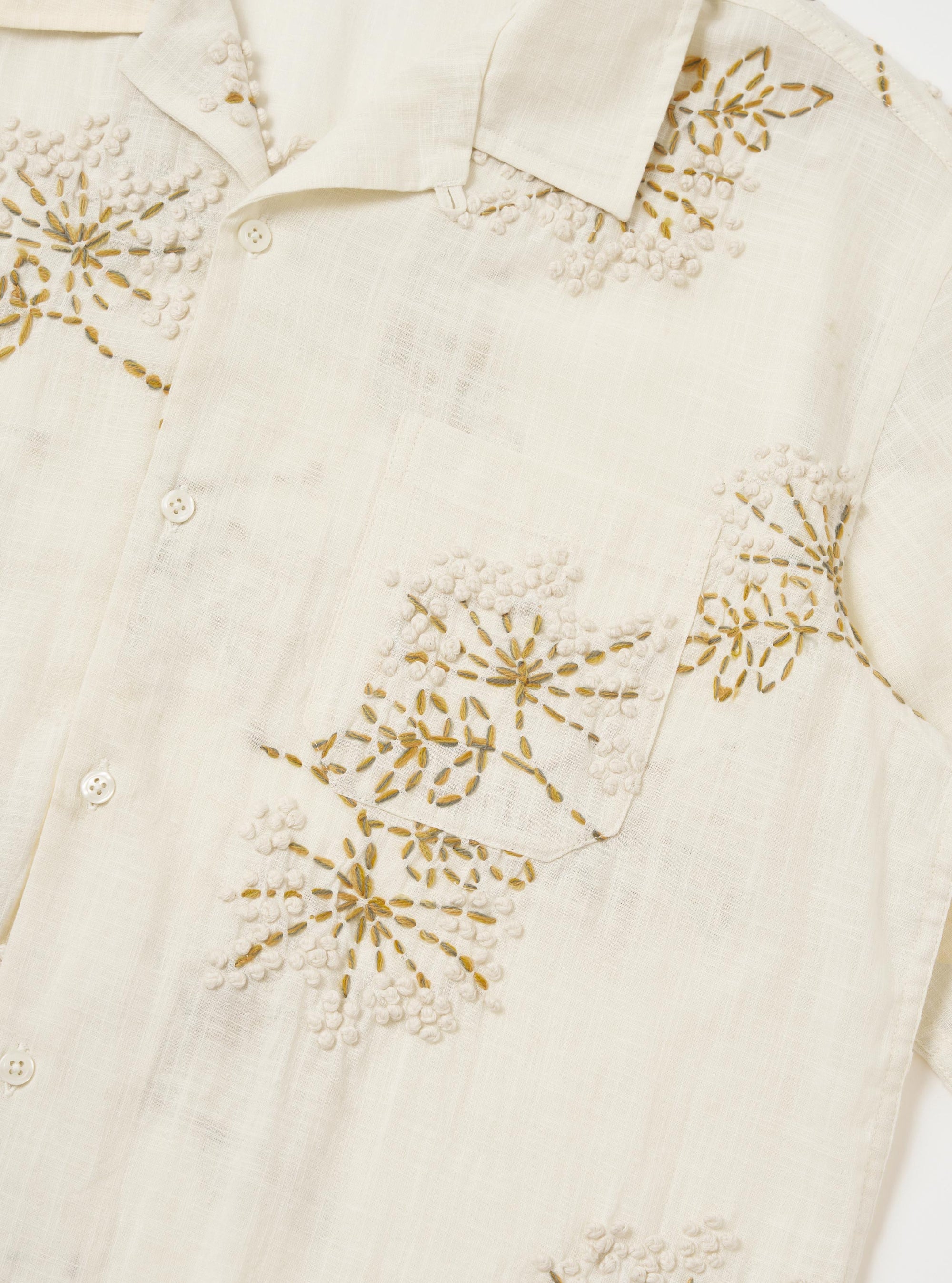 An Ecru Hand Embroidered Cotton Road Shirt is displayed flat against a plain white background. The shirt features a camp collar, a button-down front, and a single chest patch pocket on the left side. Hand-embroidered floral motifs are scattered across the ecru fabric.