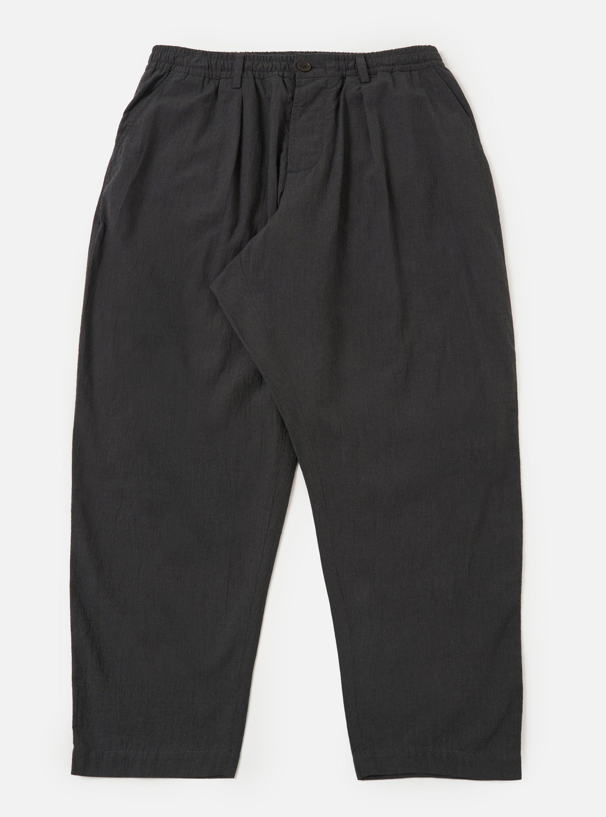 A pair of charcoal grey cotton pleated track pants is displayed flat against a plain white background. The trousers feature an elasticated waistband with a drawstring, a single pleat at the front of each leg, and side pockets.